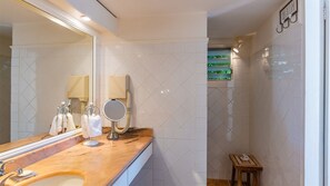 A bathroom with a large mirror, a sink with toiletries, a handheld mirror, and a shower area with a view of the outdoors. - Alizee d'Eden (1/2 Rooms) (Pointe Milou)