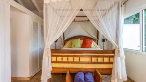 A bed with a wooden frame and a canopy, pillows in various colors, and a basket with towels at the foot of the bed. - Alizee d'Eden (1/2 Rooms) (Pointe Milou)