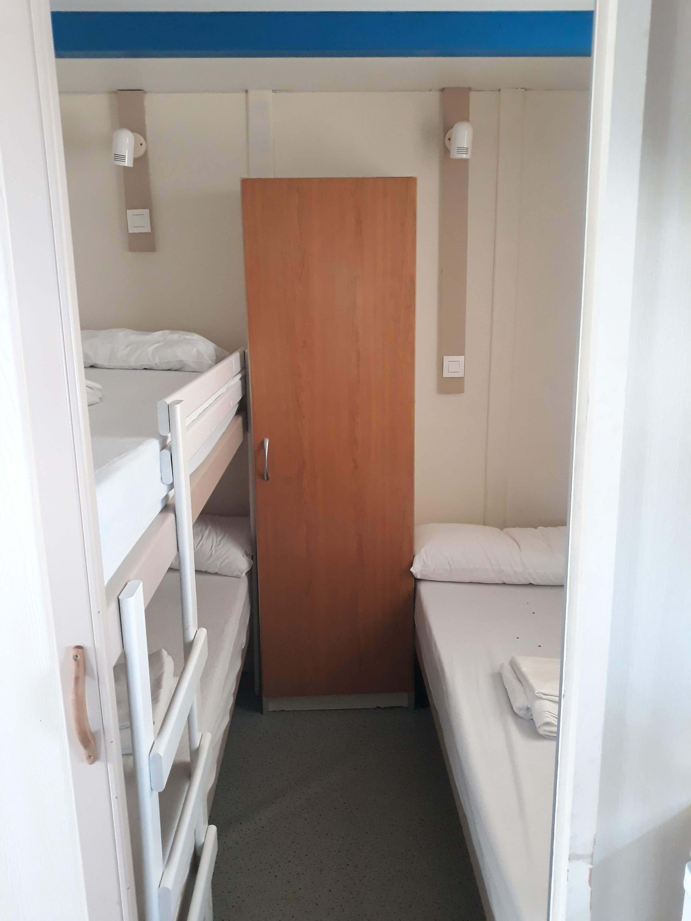 Een kleine kamer met twee bedden, een houten deur en een witte radiator.