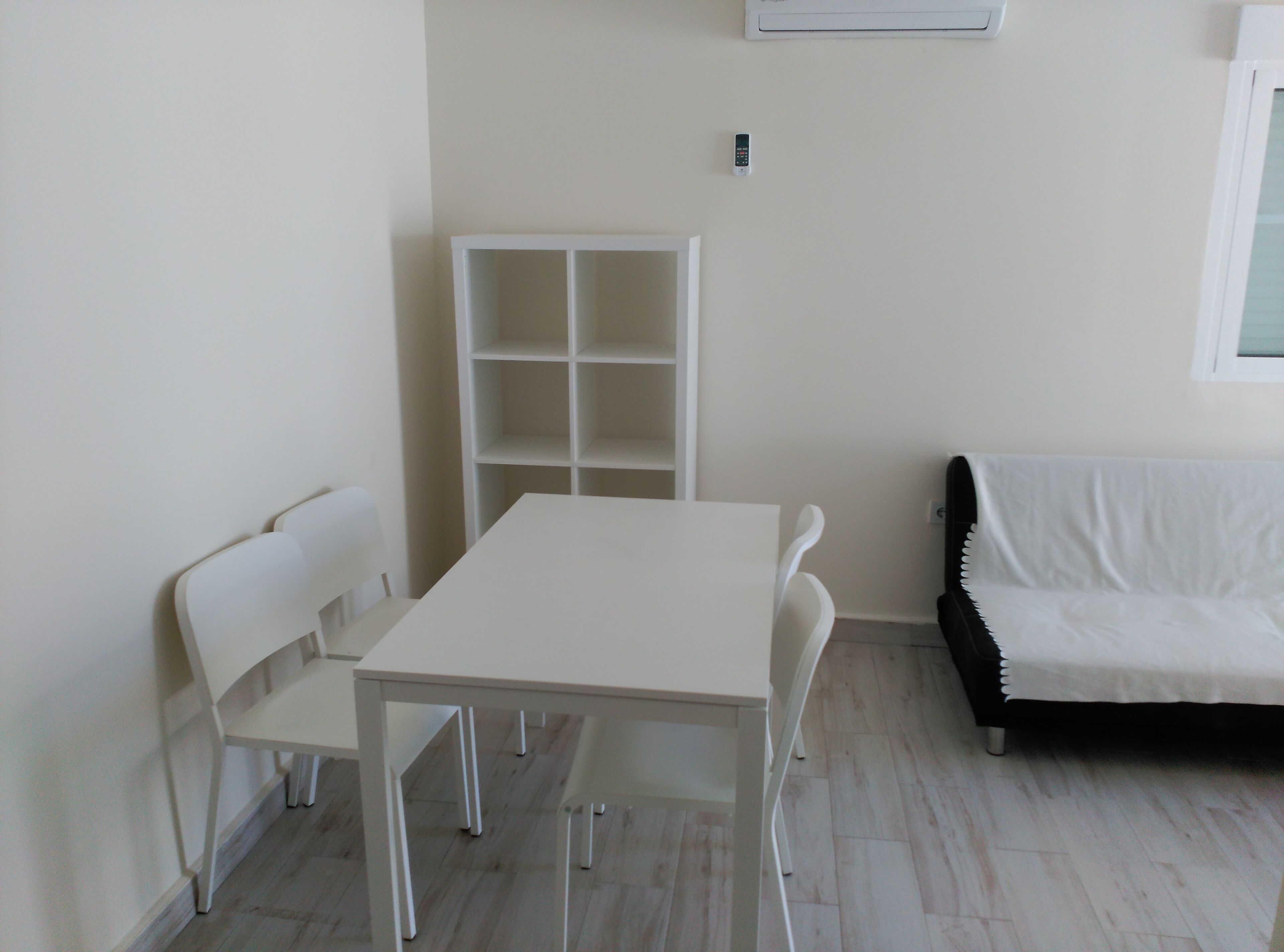 Una habitación con una mesa y sillas blancas, un sofá blanco y una estantería blanca.