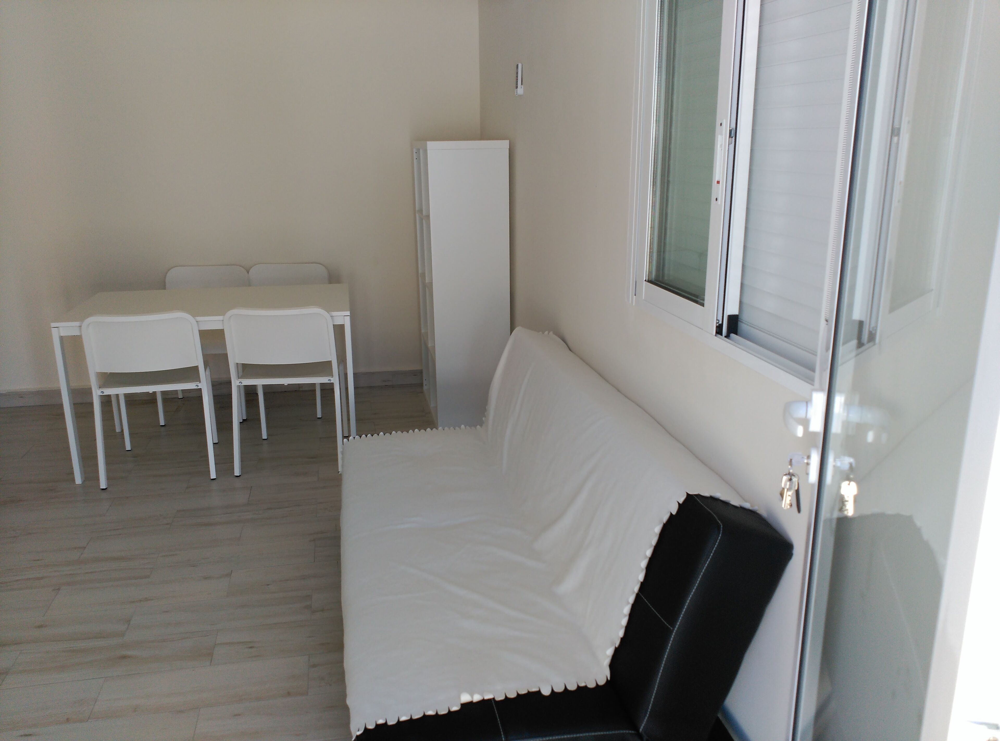 Una habitación con un sofá blanco, una mesita con dos sillas y un armario alto.