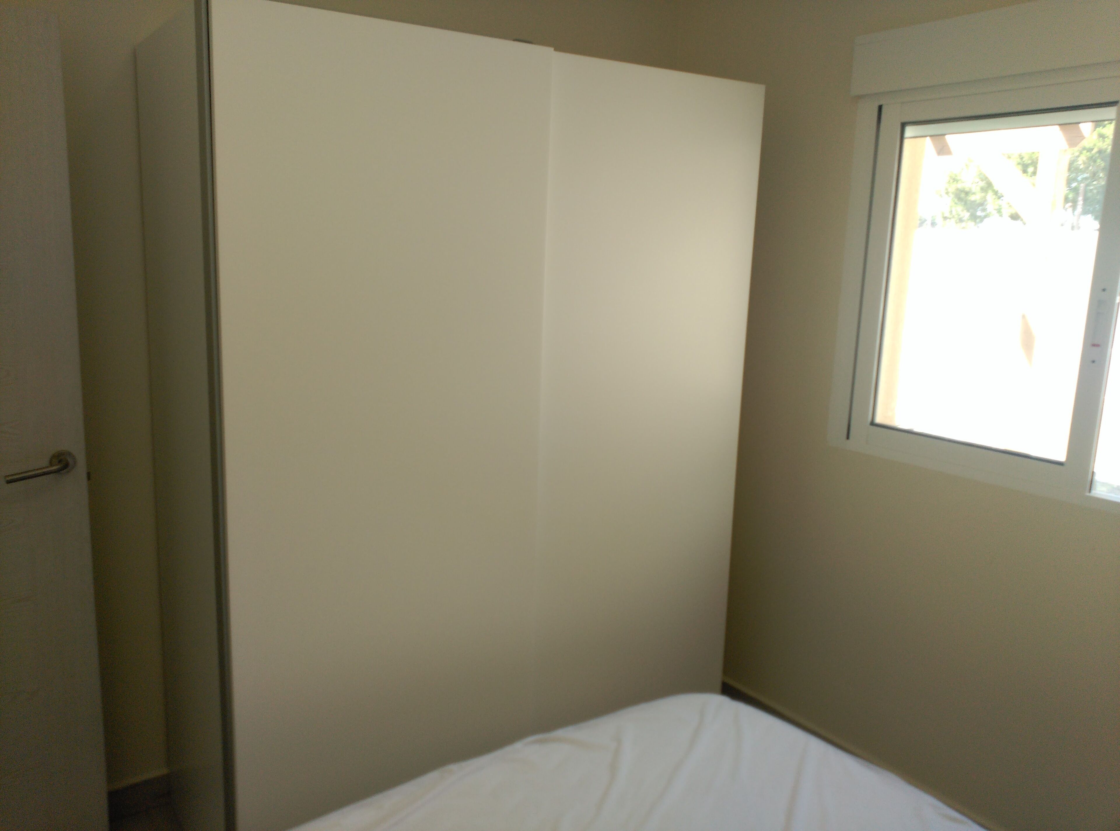 Een slaapkamer met een enkel bed, een garderobe en een raam met uitzicht op groen.