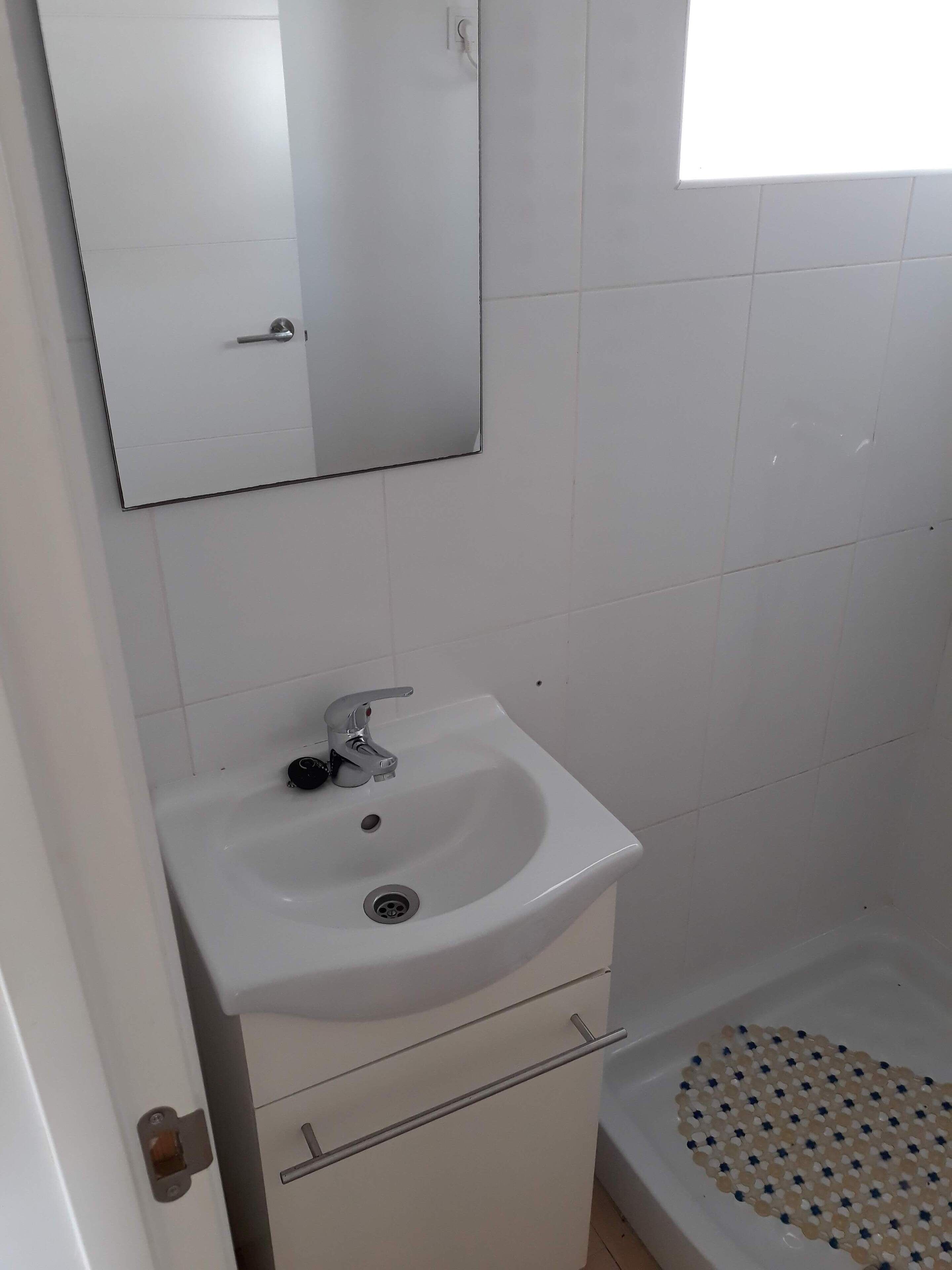 Un baño con lavamanos blanco, un espejo encima y una zona de ducha con suelo de baldosas.