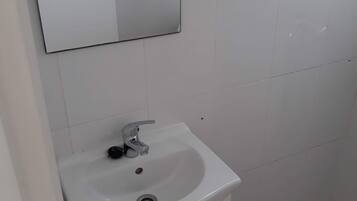 Un baño con lavamanos blanco, un espejo encima y una zona de ducha con suelo de baldosas.