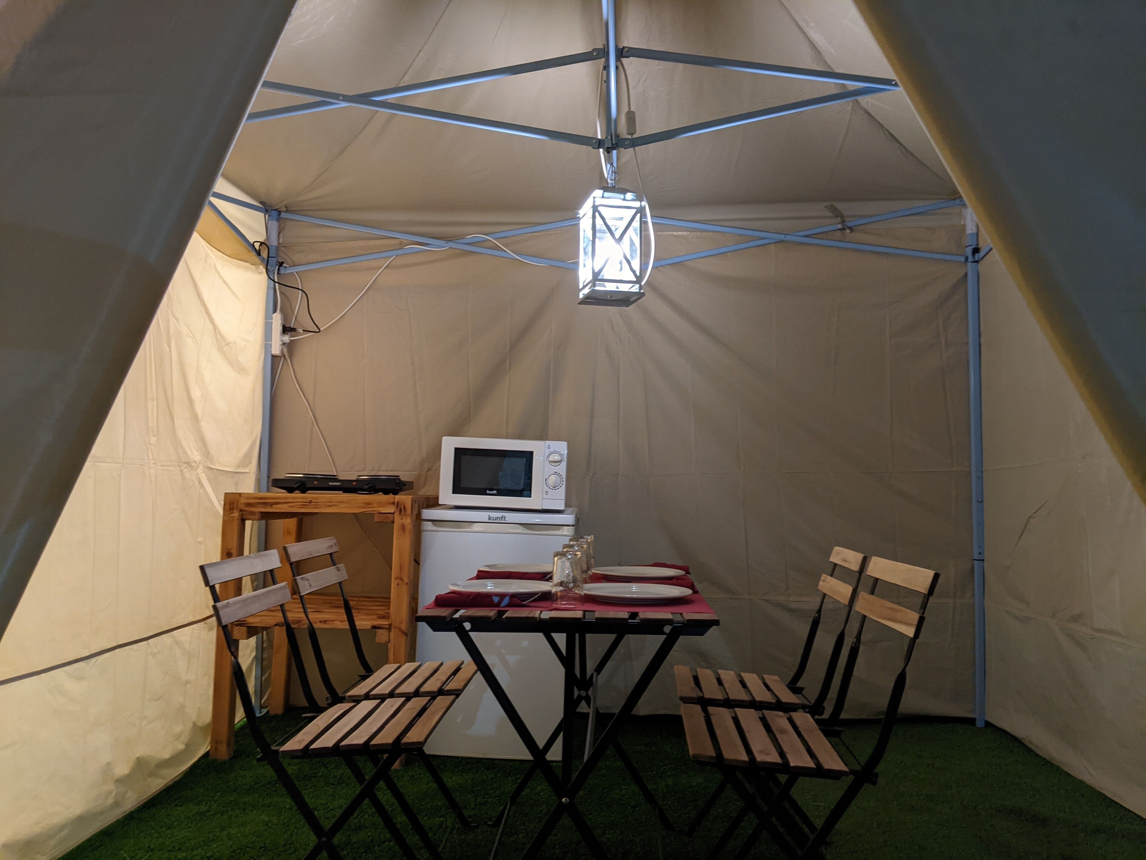 A tent with a table and chairs, a microwave, and a lantern.