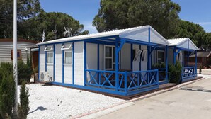 A small, single-story building with a blue exterior and white walls, featuring a porch with a railing and a small garden area with white gravel and red bricks. - camping san javier (San Javier)