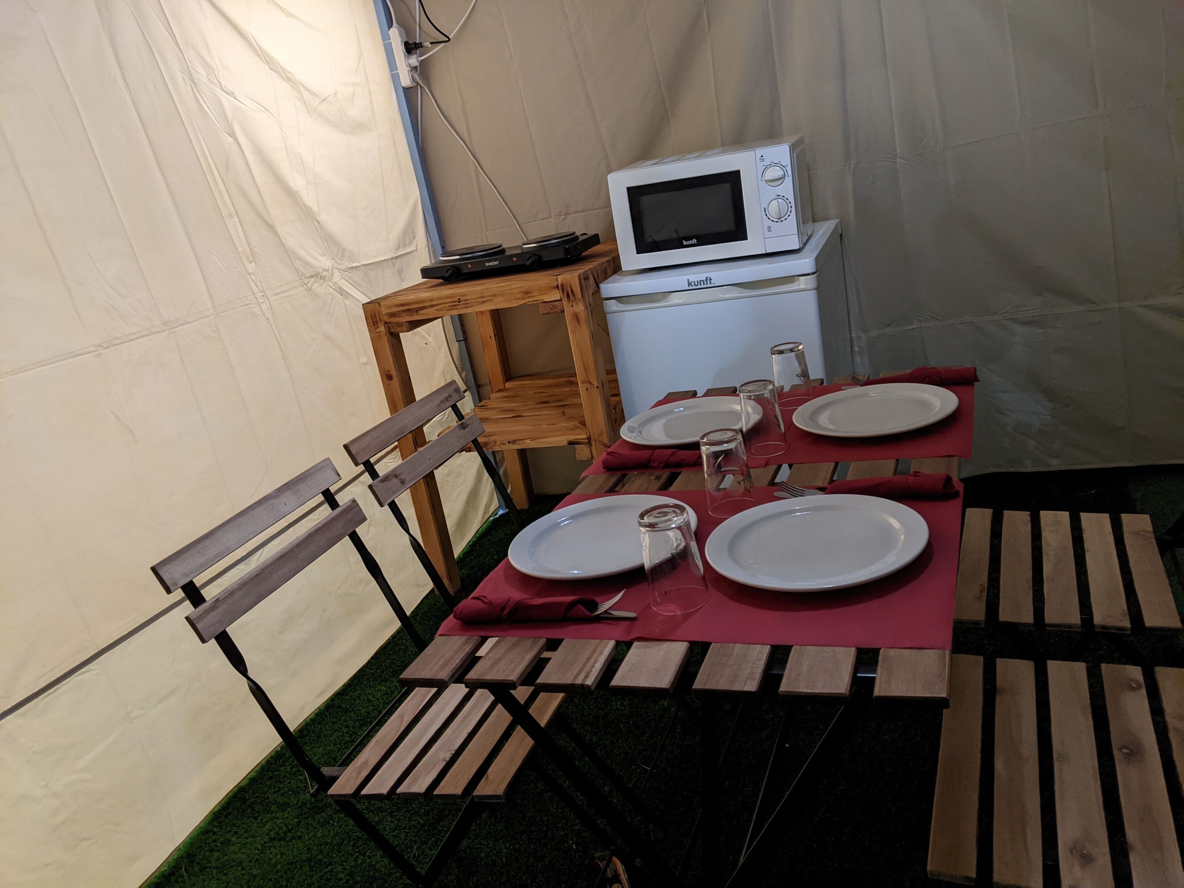 Un comedor con toldo, una mesa dispuesta para cuatro personas, un microondas y una pequeña mesita de madera.