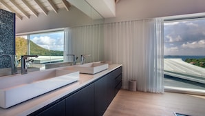 Uma casa de banho moderna com duas pias grandes, um espelho amplo e vista para a paisagem costeira.