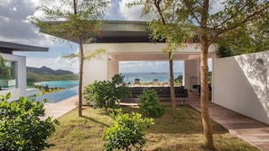 Uma área externa moderna com piscina, cadeiras de descanso e vista para o oceano.