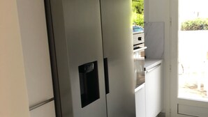 Una cocina moderna con un refrigerador de acero inoxidable integrado, armarios blancos y vistas al exterior a través de una puerta de cristal.