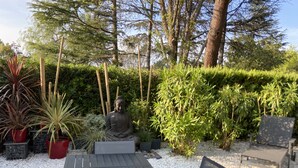 Un jardín con una estatua de Buda, plantas en macetas y una mesa de madera.