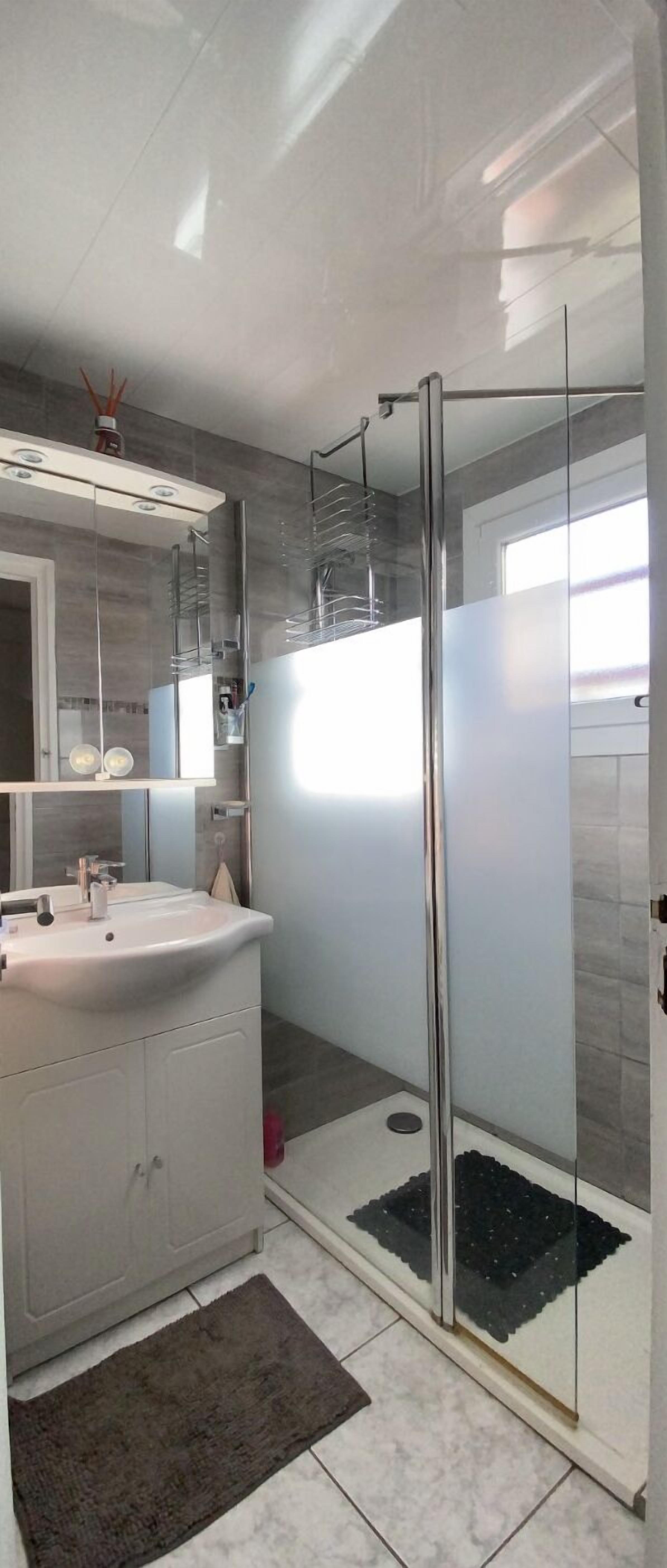 Een moderne badkamer met een douchecabine van glas, een witte wastafel en een grote spiegel boven het aanrecht.