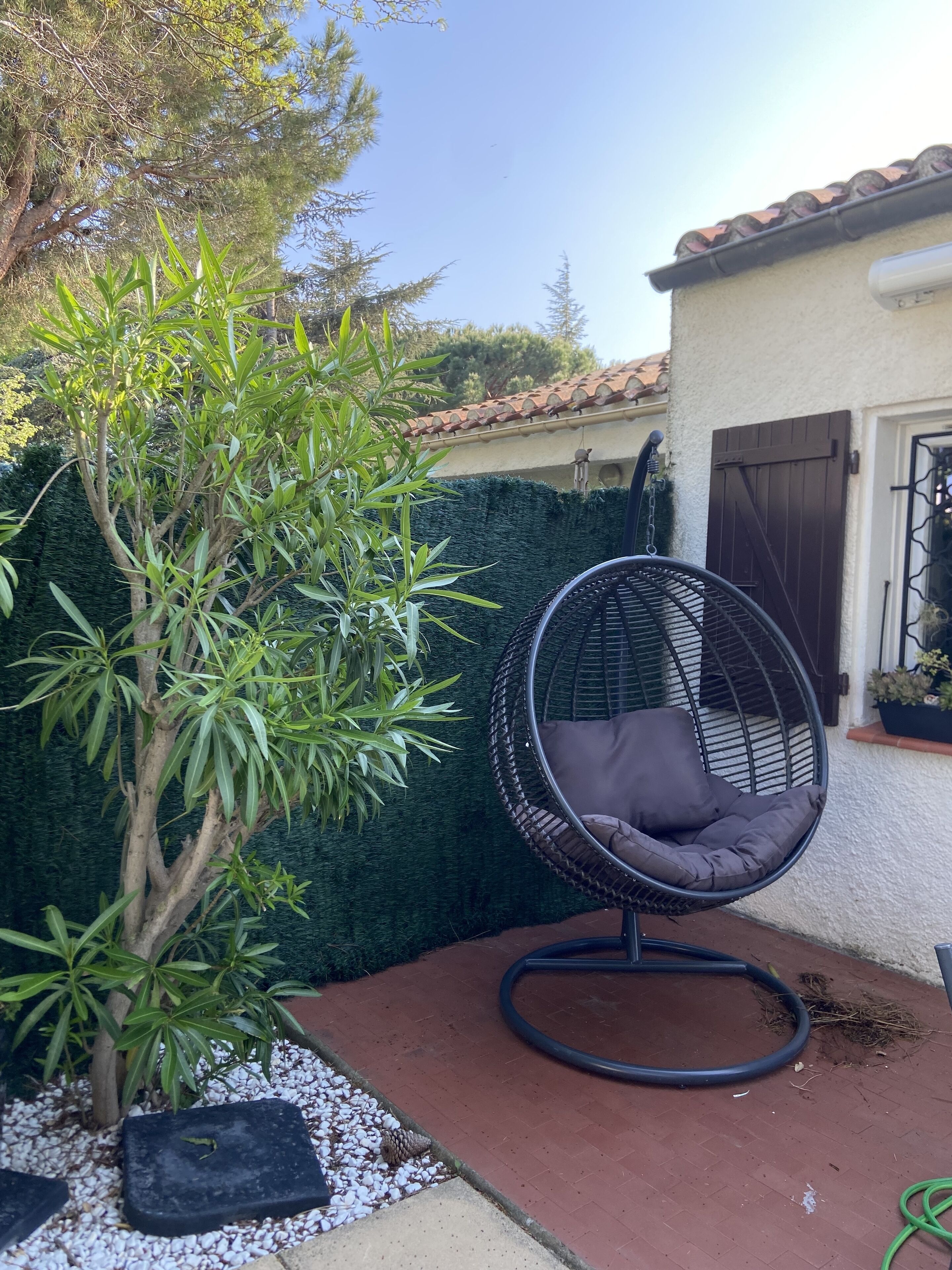 A patio area with a hanging chair, a tree, and a house with a tiled roof.