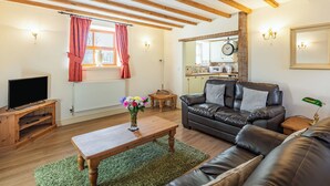 Ein gemütliches Wohnzimmer mit Holzboden, einem Ledersofa, einem Couchtisch aus Holz und einem Fernseher auf einem Holzständer.