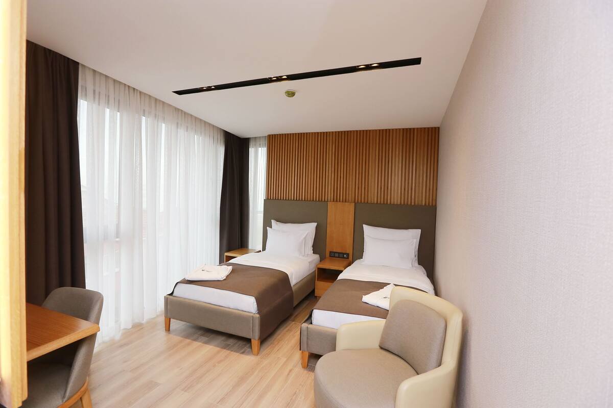 Quarto de hotel com duas camas, uma escrivaninha e uma cadeira.