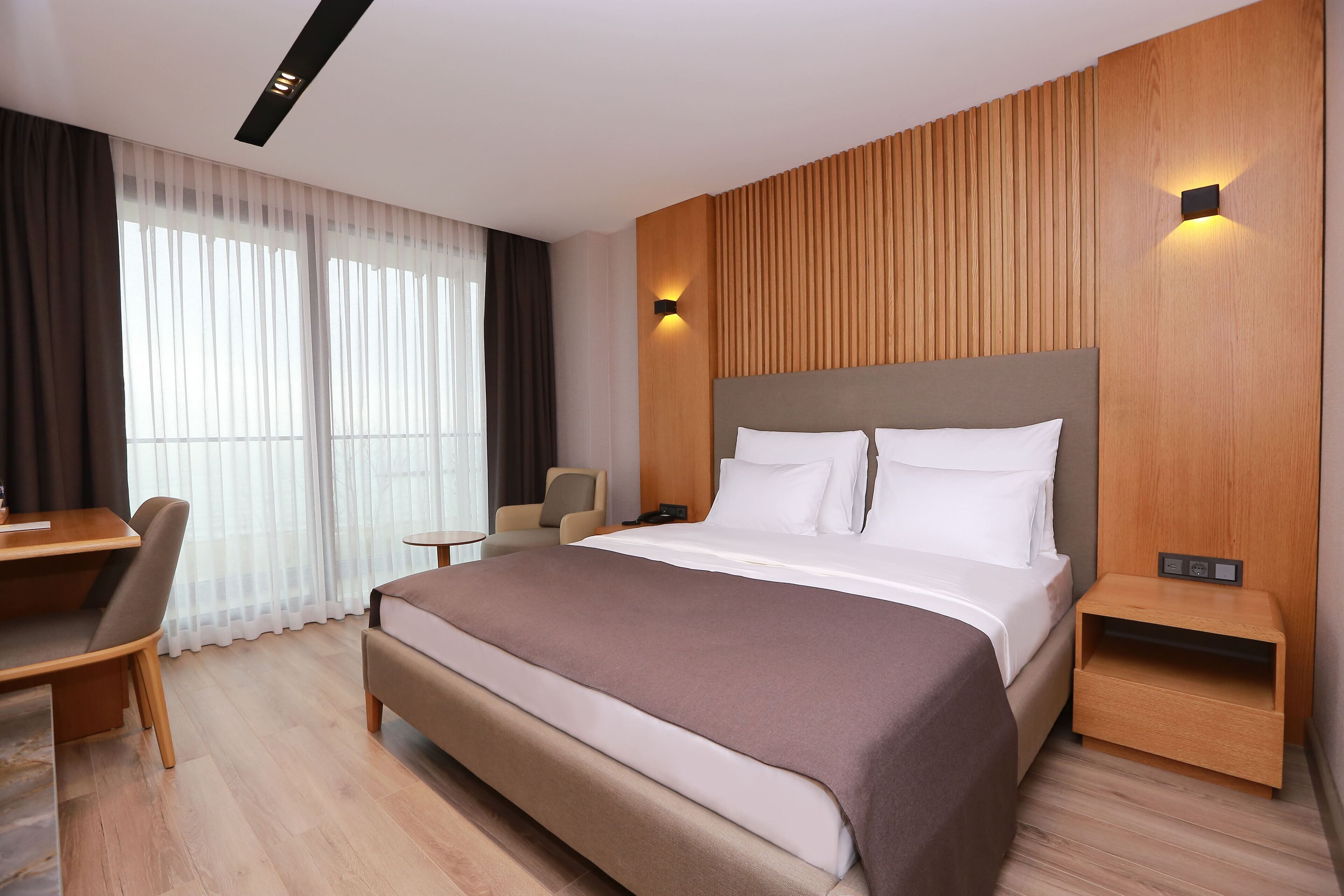 A modern hotel room with a large bed, a desk, and a chair.