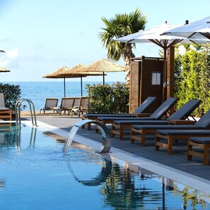 A pool area with lounge chairs and umbrellas, a clear view of the ocean, and a thatched umbrella structure. - Pikola Otel (Ordu)