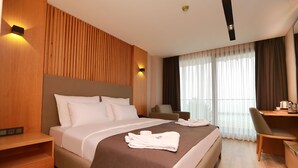 A modern hotel room with a large bed, a desk, and a chair. There are two wall-mounted lights and a window with curtains. - Pikola Otel (Ordu)