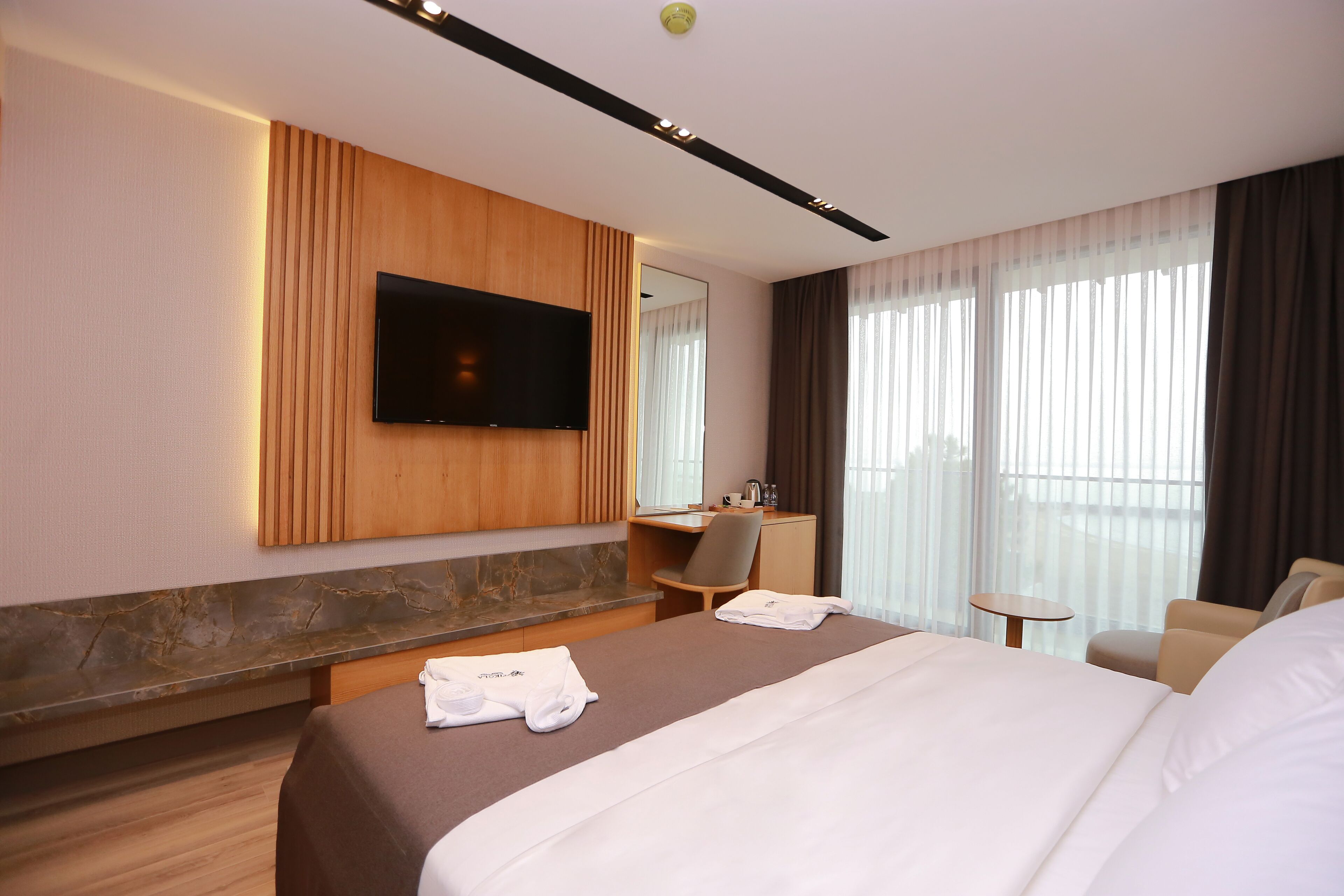 A hotel room with a large bed, a desk, a chair, a TV mounted on the wall, and a small table.