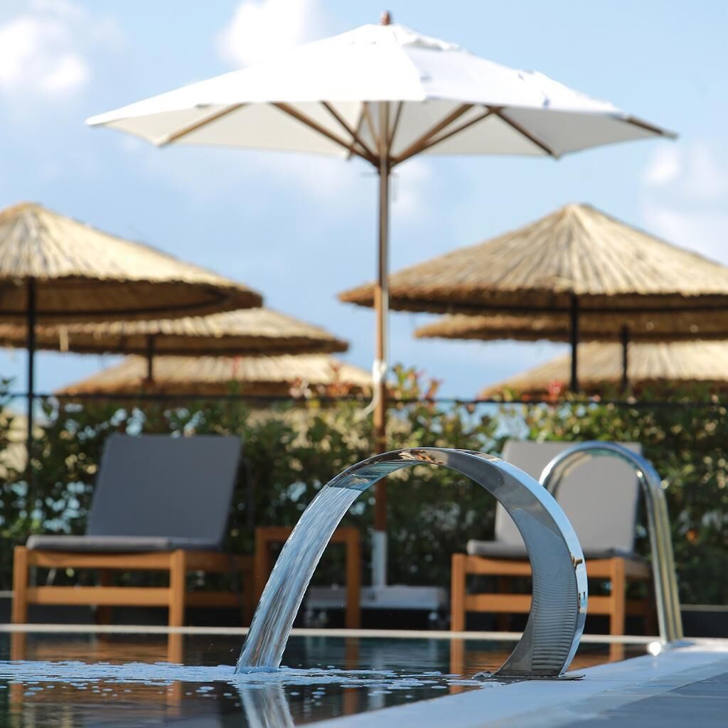 A pool area with a clear water feature, lounge chairs, and thatched umbrellas.