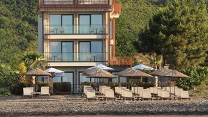 A modern two-story building with balconies, a pool area with sun loungers and umbrellas, and a view of a hillside. - Pikola Otel (Ordu)