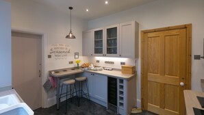 A compact kitchen with a built-in wine rack, bar stools, and a wooden door. - Chynance (Penzance)