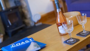 A wooden table with a bottle of wine, two wine glasses, and a brochure titled "COAST". - Chynance (Penzance)