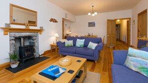 A cozy living room with a fireplace, a sofa, a coffee table, and a dining area. - Chynance (Penzance)