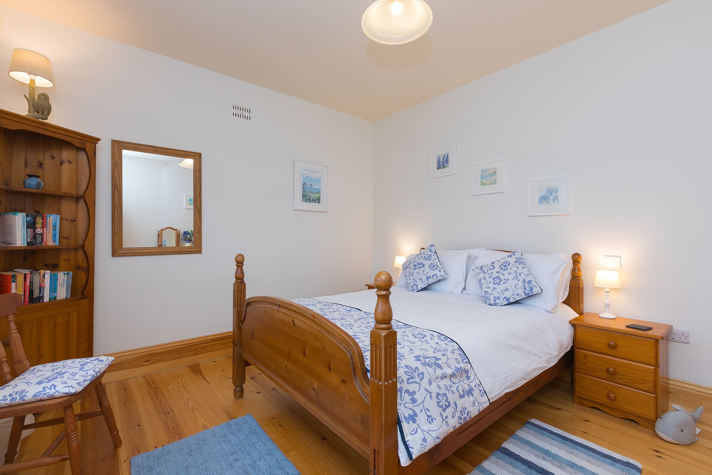 A bedroom with a wooden bed, bedside table, lamp, and a bookshelf.