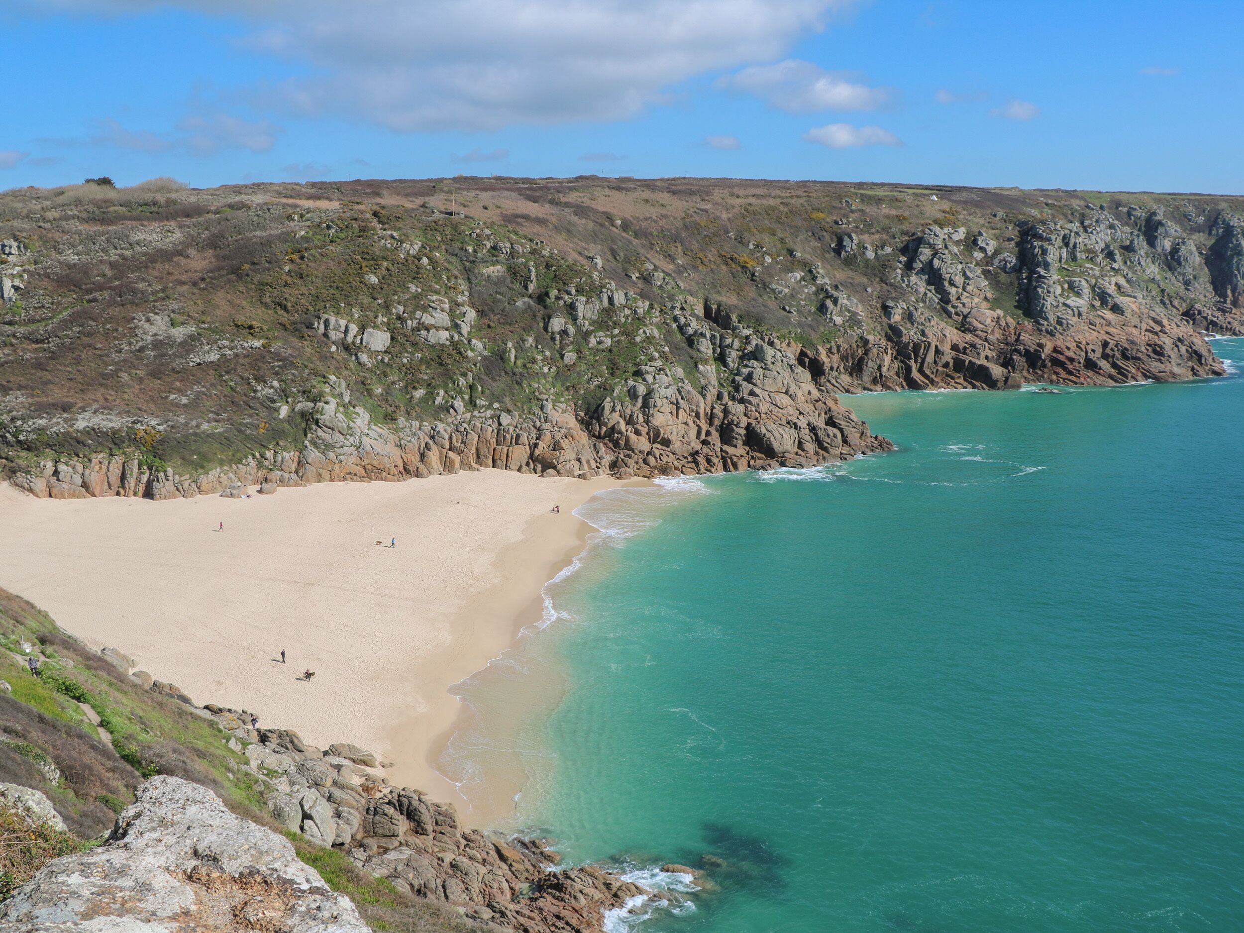 Un paysage côtier caractérisé par une plage de sable, des falaises rocheuses et des eaux turquoise limpides.
