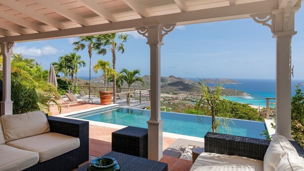 Un espacio exterior cubierto con piscina, sillones de descanso y vista al océano.