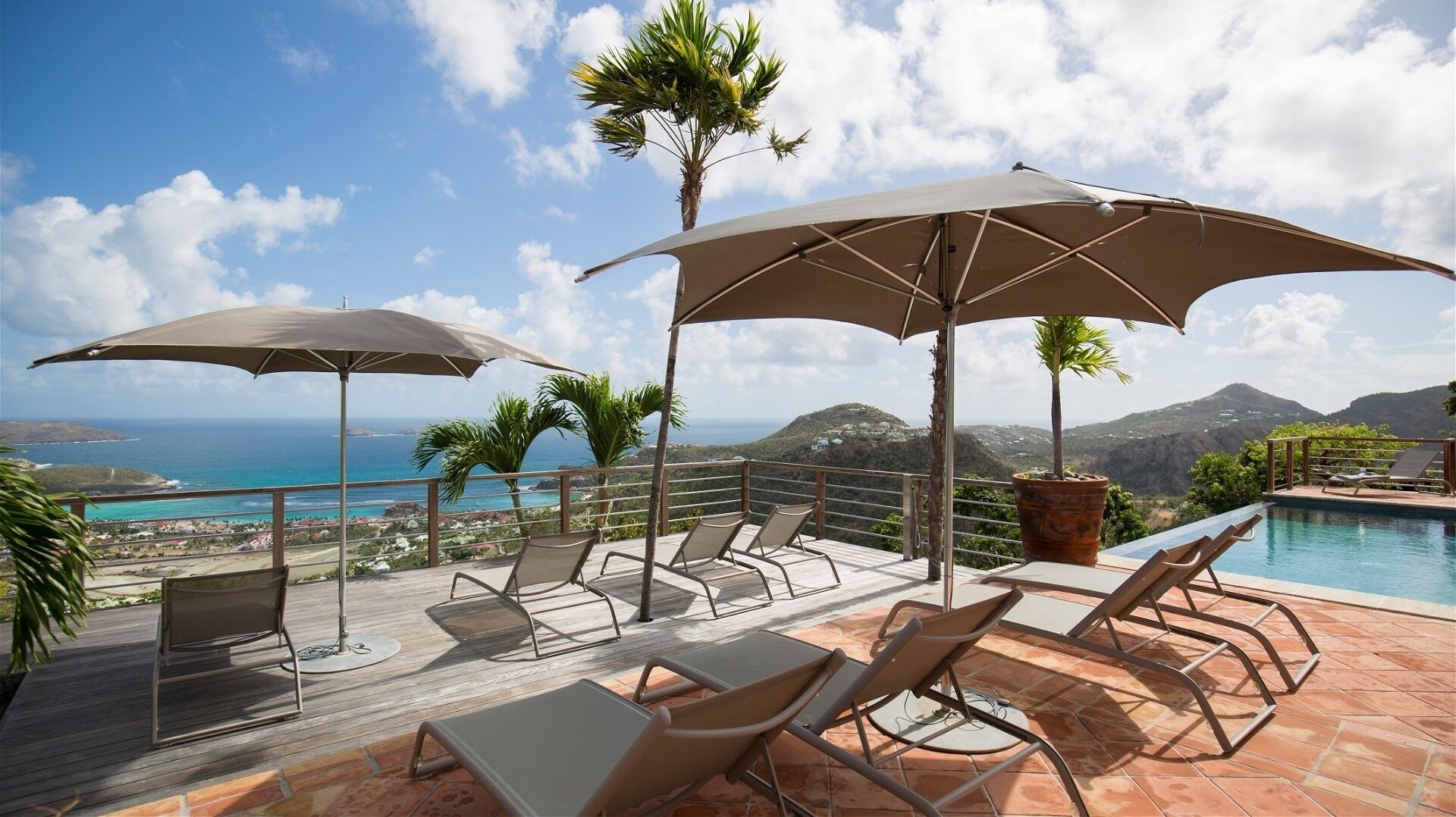 A rooftop pool area with lounge chairs and umbrellas, overlooking a coastal landscape.