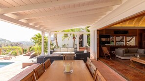 Un espace extérieur abrité, aménagé pour les repas, avec une piscine, des meubles en osier et une vue sur les collines.