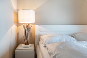 A neatly made bed with white linens and a modern lamp with a wooden base on a white nightstand. - Apartment "Casa 50" with Garden & Shared Pool (Gargnano)