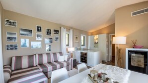 A modern living room with a striped sofa, a dining table with decorative items, a kitchen area, and a wall adorned with framed photographs. - Apartment "Casa 50" with Garden & Shared Pool (Gargnano)