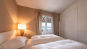 A hotel room with a bed, a nightstand with a lamp, a window with curtains, and a view of the outdoors. - Apartment "Casa 50" with Garden & Shared Pool (Gargnano)