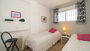 Un dormitorio con dos camas, una silla, un escritorio, una lámpara y una ventana con cortinas.