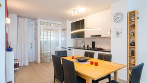 Una cocina moderna con comedor, un reloj en la pared y una estantería de madera con objetos decorativos.
