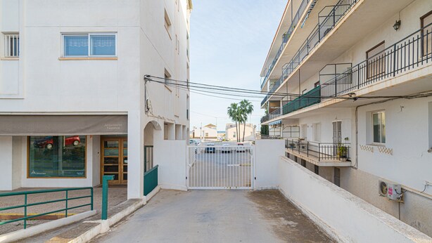 Una calle estrecha flanqueada por edificios, una entrada con portón y una tienda con letrero a la vista.