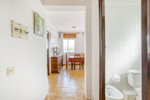 Un couloir mène à une salle à manger où se trouvent une table et des chaises, un buffet en bois et une fenêtre avec des rideaux.