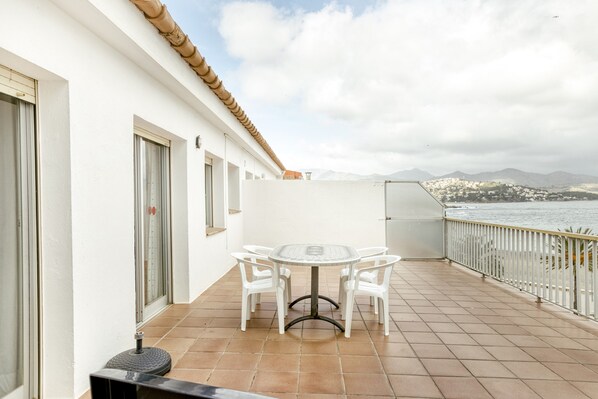 Een balkon met een tafel en stoelen, uitzicht op zee en bergen in de verte.