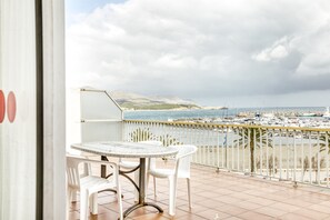 Een balkon met een tafel en stoelen, met uitzicht op een jachthaven vol boten en een berg in de verte.