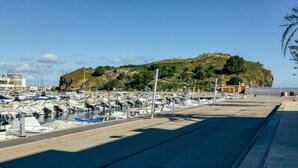 Una marina con barcos amarrados, un edificio con señalización y una colina con vegetación al fondo.