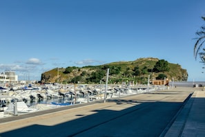 Un port de plaisance avec des bateaux amarrés, un ciel dégagé et, au loin, une colline sur laquelle se dressent des ruines.