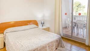 A bedroom with a bed, nightstand, lamp, and a sliding glass door leading to an outdoor area with chairs. - Apartment on the Paseo Marítimo '1-3' close to the Beach with Terrace & Wi-Fi (Llançà)