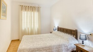 A bedroom with a bed, a nightstand, a lamp, a window with curtains, and a wall-mounted light fixture. - Apartment on the Paseo Marítimo '1-3' close to the Beach with Terrace & Wi-Fi (Llançà)