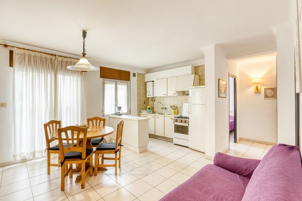 A compact kitchen with white cabinets, a dining table with chairs, and a purple sofa.