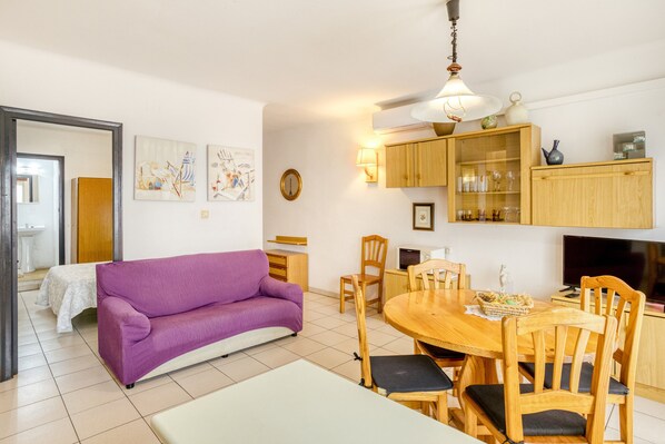 A room with a purple sofa, wooden dining table, chairs, a TV, and cabinets.