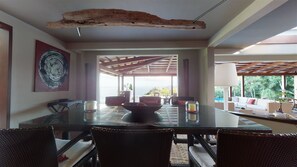 Un coin repas avec une table en verre, des chaises en osier et une vue sur l’océan.