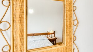 A mirror with a woven frame, a wooden bedside table, a lamp, and a patterned bedspread. - Apartment 'Mediterranean View 3-1' close to the Beach with Terrace & Wi-Fi (Llançà)